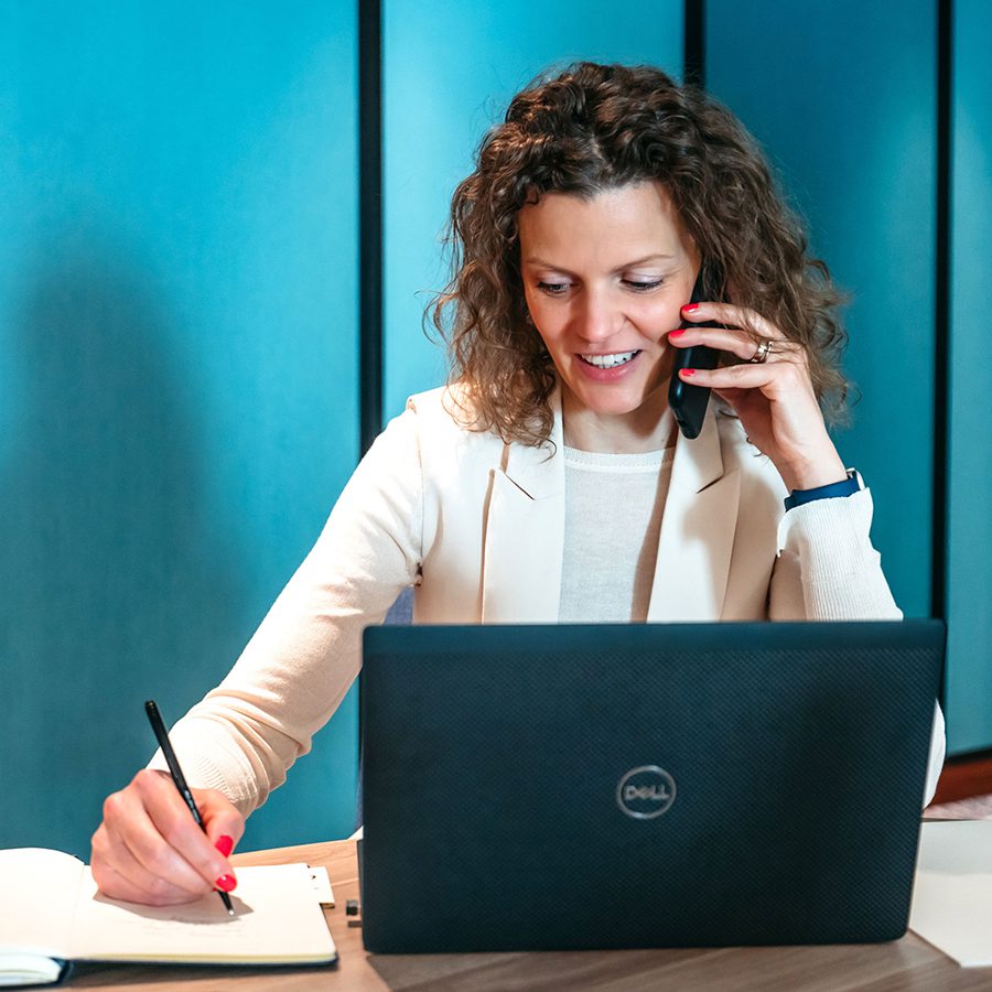Curly haired White woman on cellphone with laptop